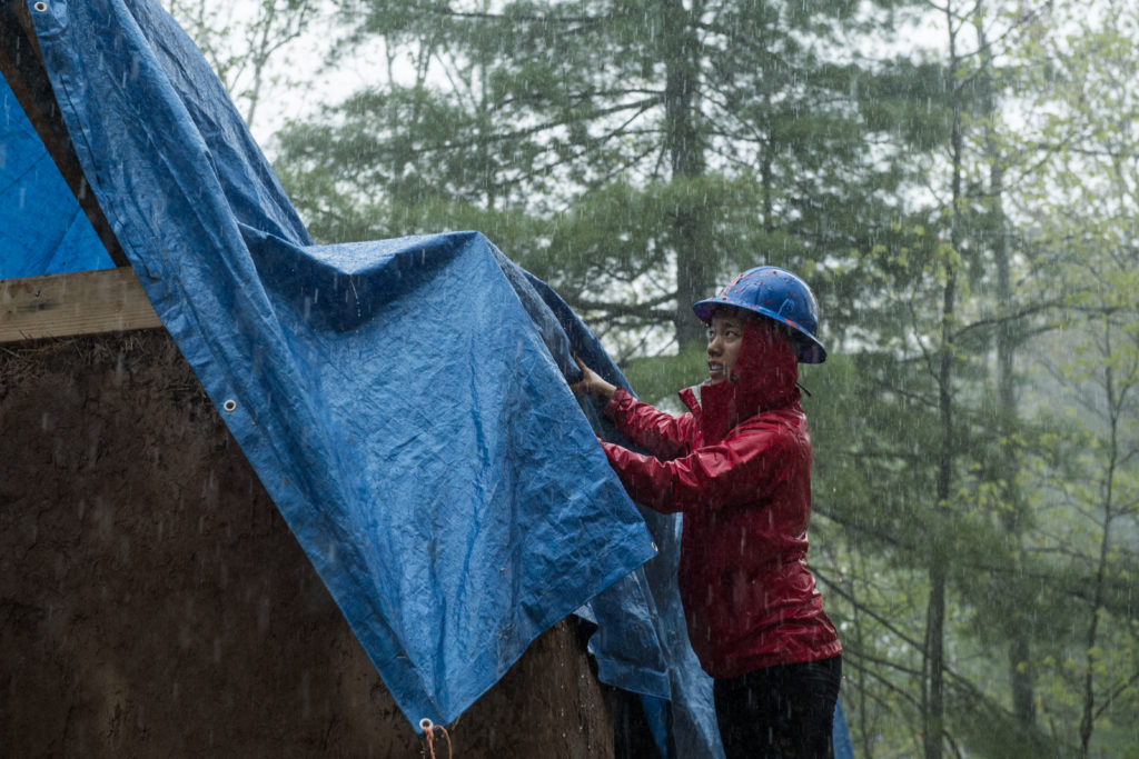 Un estudiante cubre la construcción para proteger la paja de la lluvia.