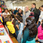 Estudiantes de En Nuestra Lengua pasan por las diferentes mesas en Bach Elementary durante la recaudación anual de fondos para el programa, que incluye la venta de comidas típicas de países de habla hispana. Peter Matthews, Michigan Photography.