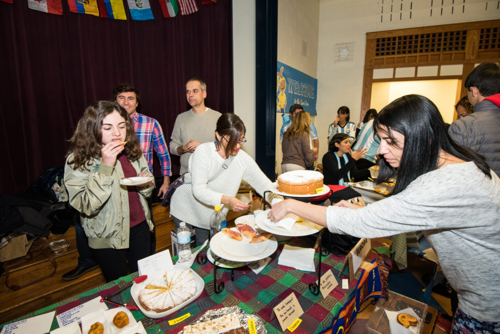 Padres y miembros de la comunidad participant en la recaudación annual de fondos para el programa En Nuestra Lengua, que incluye la venta de comidas típicas de países de habla hispana preparada por los mismos padres.