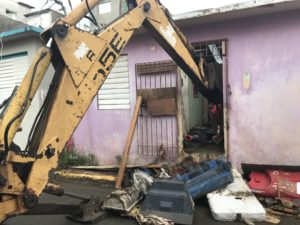 Voluntarios usan una excavadora para limpiar una casa abandonada que, debido a su proximidad con otras casas, se había convertido en la fuente de la plaga de mosquitos y ratas para el resto del vecindario.