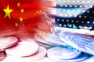 Banderas de EE. UU. y China en monedas y gráfico del mercado de valores, simbolizando la guerra comercial de aranceles económicos y barreras fiscales entre Estados Unidos de América y China. Crédito de la imagen: iStock.