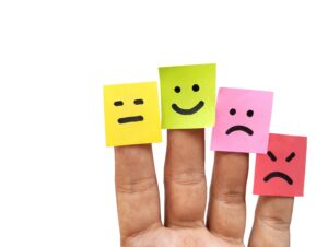 Emoji feliz, neutral, triste y enojado sobre papeles adhesivos de colores pegados a los dedos. Concepto de salud mental, cambios de ánimo, depresión y trastorno bipolar. Crédito de imagen: Adobe Stock