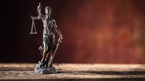 Figura de bronce de la Dama de la Justicia sosteniendo una espada y una balanza sobre una mesa de madera. Crédito de imagen: Adobe Stock