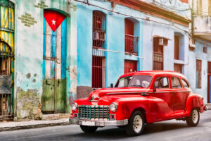Auto clásico y edificio antiguo con la bandera cubana en La Habana Vieja. Foto: kmiragaya / Adobe Stock.